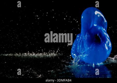 Palloncino d'acqua deformato che colpisce una lastra di vetro bagnata con acqua su uno sfondo scuro. Foto Stock
