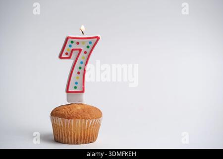Cupcake di compleanno con la candela numero 7 accesa su sfondo bianco Foto Stock