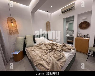 Letto d'albergo non fatto con piumone beige ondulato, cuscini decorativi e lampade in vimini. Vista sul bagno moderno. Concetto di viaggio e alloggio. Foto Stock