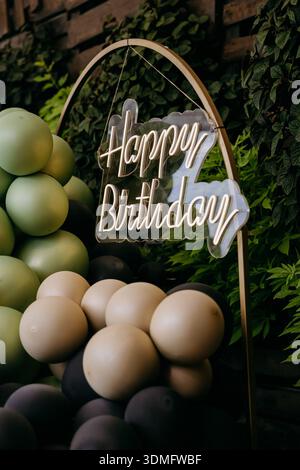 Cartello al neon Happy Birthday con arco a palloncino verde e decorazioni per feste all'aperto Foto Stock