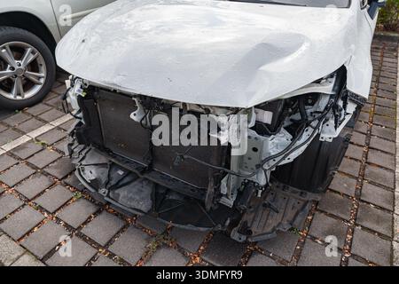 Vettura bianca gravemente danneggiata con radiatore e telaio esposti dopo una collisione frontale Foto Stock