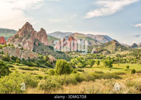 Una catena montuosa con una grande formazione di roccia rossa al centro. Il cielo è limpido e il sole splende Foto Stock