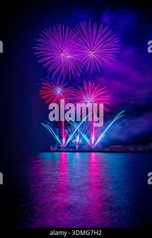 I colorati fuochi d'artificio esplodono sull'acqua di notte, creando vivaci riflessi sulla superficie e illuminando il cielo in una festa festosa. Foto Stock