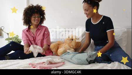 Donne pieghevoli che indossano camicie nere rosa, zaino azzurro sul letto, con orsacchiotto tintinnato Foto Stock
