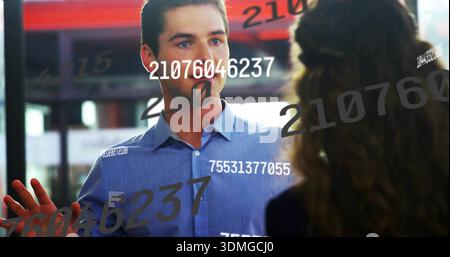 Uomo che preme in camicia azzurra, con palmo su divisorio in vetro in ufficio, con sovrapposizioni numeriche Foto Stock