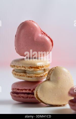 Tre macaron a forma di cuore sono impilati uno sopra l'altro. Il macaron superiore è rosa, mentre gli altri due sono beige e rosa chiaro. Foto Stock
