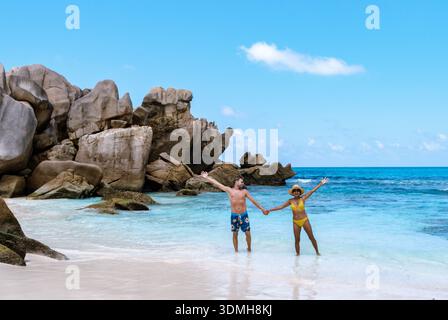 Trascorrendo una giornata di pace alla spiaggia di Anse Cocos, una coppia si trova mano nella mano nelle acque azzurre di la Digue Seychelles, circondati da splendidi graniti Foto Stock