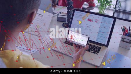 Tenendo in mano il telefono, uomo in camicia gialla che esamina il rapporto del portatile con un collega con la giacca rossa sui documenti della scrivania Foto Stock