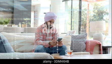 In mano uno smartphone, un uomo indiano in un turbante rosa che tocca lo schermo nella moderna lounge con sovrapposizione digitale Foto Stock
