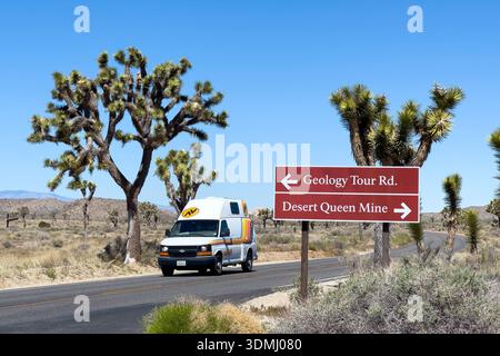 Camper in auto lungo la strada panoramica di Park, oltre gli alberi di Joshua e un cartello stradale nel Joshua Tree National Park, California Foto Stock