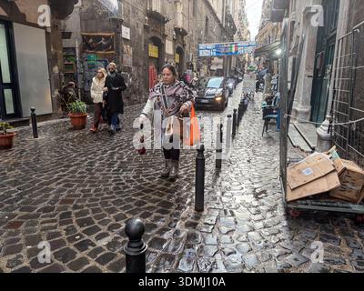 Strada acciottolata bagnata (sanpietrini) nell'affollato centro storico (Centro storico) di Napoli, Italia. Pedoni e traffico di veicoli in vicoli stretti Foto Stock