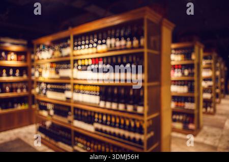 Scaffali alti con bottiglie fullate di bevande alcoliche d'élite nella grande cantina di enoteca, foto sfocata. Foto Stock