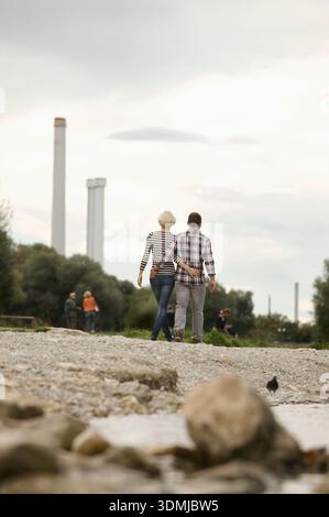 Vista posteriore di una giovane coppia che cammina insieme su un fiume roccioso Foto Stock