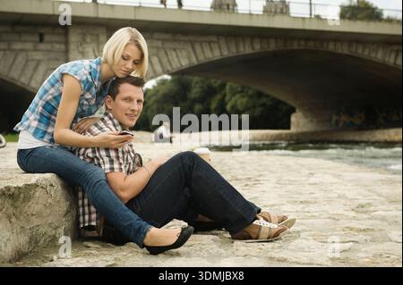 Coppia affettuosa che si coccola sulla riva del fiume in pietra sotto il ponte della città Foto Stock