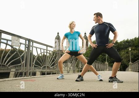 Giovane coppia atletica che si allunga insieme sul ponte Foto Stock