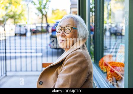 Ritratto di una donna asiatica anziana seduta fuori da un negozio Foto Stock