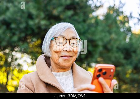 Donna asiatica anziana che usa il suo telefono nel parco Foto Stock