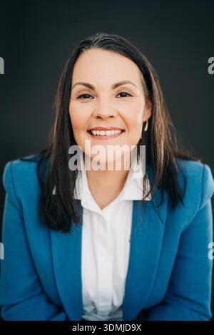 Donna sorridente con blazer blu che si piega in avanti con un'espressione calda Foto Stock