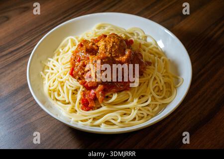 Piatto di spaghetti condito con polpette e ricca salsa di pomodoro servito su un tavolo di legno. Foto Stock