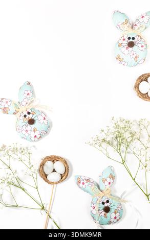 Tre cuccioli decorativi di Pasqua realizzati in tessuto con motivi floreali, piccole uova e delicati fiori bianchi disposti su un fondo bianco pulito, Foto Stock