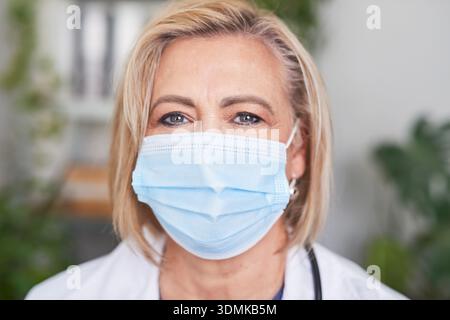 Professionista sanitario femminile senior che indossa una maschera medica in un ambiente all'aperto Foto Stock