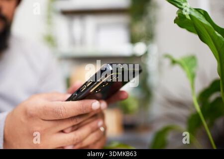 Primo piano di mani che tengono lo smartphone in Un ambiente indoor per le aziende pieno di impianto Foto Stock