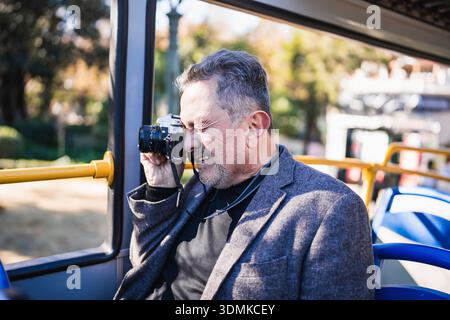 Uomo maturo che fotografa una città da un autobus turistico Foto Stock