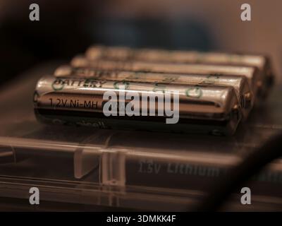 Primo piano di batterie ricaricabili AAA Ni-MH da 1,2 V disposte in fila su una custodia in plastica trasparente sotto una luce ambiente calda. Foto Stock