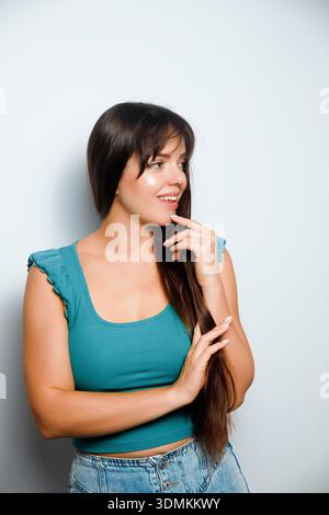 Una giovane donna si trova in uno studio, guardando al fianco con un sorriso. Ha i capelli lunghi e indossa un top blu e jeans. Foto Stock