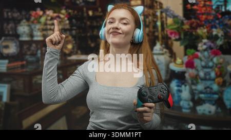 Donna che tiene in mano il gamepad e indossa le cuffie Cat Ear punta il dito indice nell'edificio; gioco divertente. Foto Stock