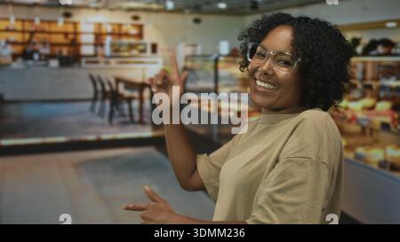 Donna afroamericana sorridente e danzante con il dito puntato in un edificio di panetteria; espressione di gioia giovanile. Foto Stock