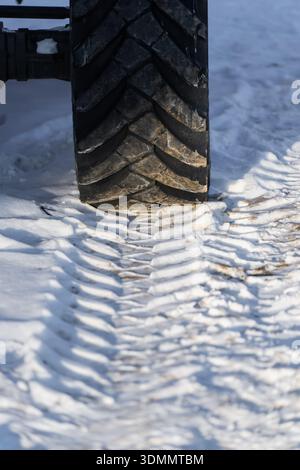 Primo piano dello pneumatico del veicolo fuoristrada su terreni innevati con battistrada profondo, tracce di carreggiata fresche e neve compressa che mostra i dettagli della trazione invernale Foto Stock