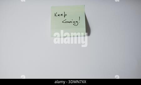 "Continua!" Scritto a mano su Green Sticky Note: Concetto aziendale di motivazione e perseveranza Foto Stock
