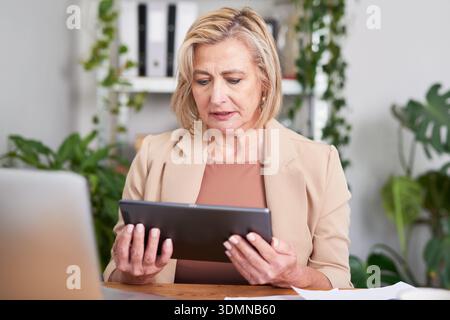 Donna d'affari che esamina tablet in un ambiente ufficio moderno con Focus e comportamento professionale Foto Stock