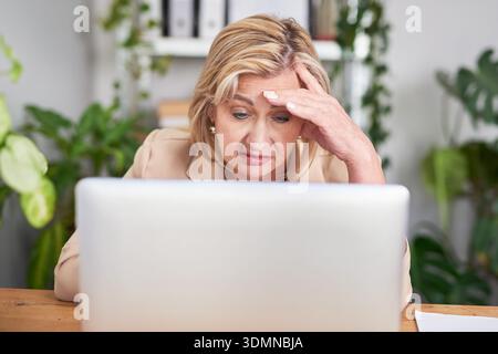Donna professionista alla scrivania che guarda stressata mentre lavora su un notebook in Bright Office Foto Stock