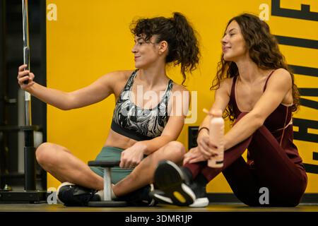 Due donne posano per un selfie mentre si fanno una pausa dall'esercizio fisico in un centro fitness nel pomeriggio Foto Stock