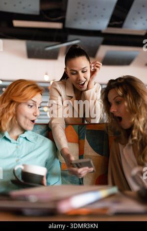 Tre donne d'affari si impegnano in una vivace discussione mentre esaminano i documenti con un caffè in un ambiente moderno durante il pomeriggio Foto Stock