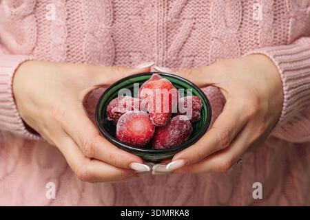 Donna che tiene le fragole congelate in un primo piano. Snack di frutta sano e concetto di cibo naturale con frutti di bosco congelati al coperto. Foto Stock