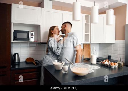 Una coppia sta vicino in una cucina mentre preparano la colazione insieme. Stanno sorridendo e si godono il loro tempo mentre interagiscono tra loro in un Foto Stock