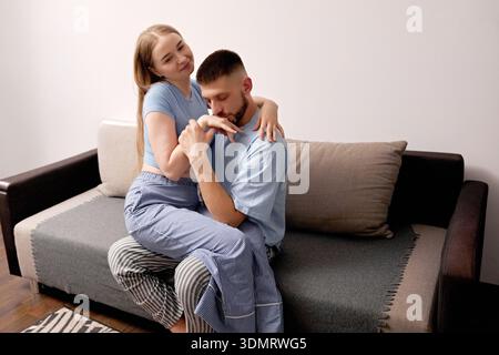 Due persone condividono un momento intimo su un divano vestito con abiti casual. Si siedono da vicino e si impegnano in una calda interazione in ambienti chiusi durante il giorno Foto Stock