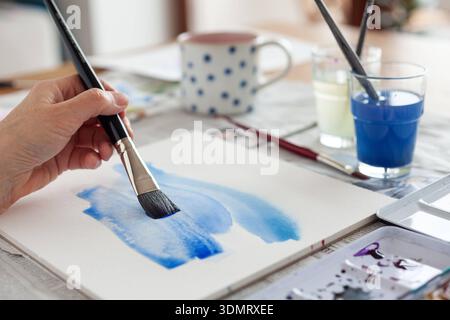 MIT Aquarellfarben malen - Frau malt mit Aquarellpinsel einen blauen Hintergrund - Jena Atelier Deutschland *** Pittura con acquerelli donna dipinge uno sfondo blu con un pennello ad acquerello Jena Atelier Germania Foto Stock