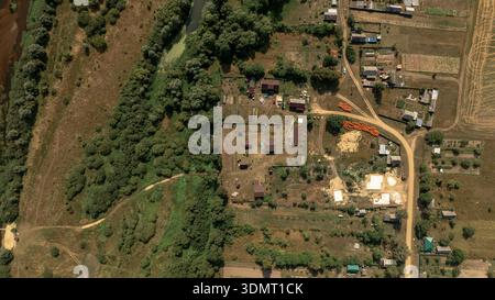 Un drone cattura una zona rurale in Bielorussia con un fiume tortuoso, una fitta vegetazione, case sparse, giardini, strade sterrate, e campi agricoli. Foto Stock