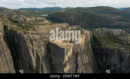 Preikestolen, una scogliera piatta in cima alla Norvegia, si affaccia sul Lysefjord con scogliere ripide, terreno lussureggiante e un piccolo lago visibile sullo sfondo. Foto Stock