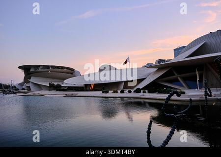Un'ampia e straordinaria immagine del Museo Nazionale del Qatar a Doha al tramonto, che mostra la sua iconica architettura ispirata alle rose del deserto che si riflette nella calma Foto Stock