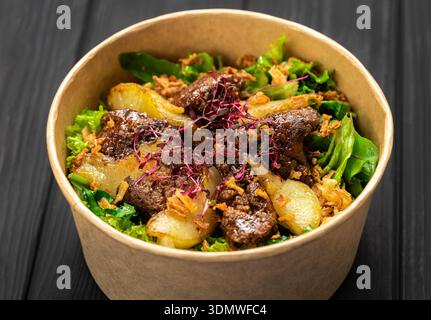 Insalata di fegato calda con pere caramellate, verdure miste e cipolle croccanti in kraft Bowl Foto Stock