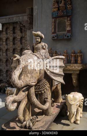 Una statua rustica di elefante in legno con intricate incisioni e' esposta su uno sfondo di decor tradizionale. Foto Stock