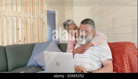 Una coppia matura pendente con camicetta rosa e camicia a righe che guarda il laptop sul divano con cuscino blu Foto Stock