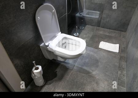 WC moderno a parete con coperchio aperto in un bagno combinato con piastrelle in ceramica grigio scuro, doccia in vetro e tappetino bianco, che mostra un design igienico pulito e interni moderni Foto Stock