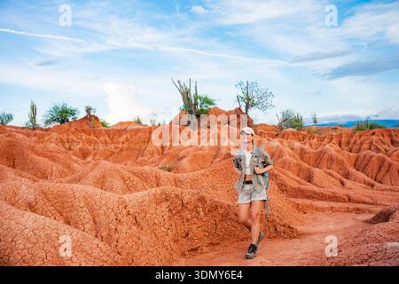 Un viaggiatore cammina attraverso le impressionanti formazioni rocciose rosse e arancioni del deserto di Tatacoa sotto un cielo azzurro limpido in Colombia, mostrando l'uniqu della zona Foto Stock
