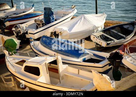 Una collezione di piccole barche attraccate in un porticciolo, crogiolandosi alla calda luce del sole. La scena cattura un tranquillo ambiente costiero con navi colorate che leggono Foto Stock